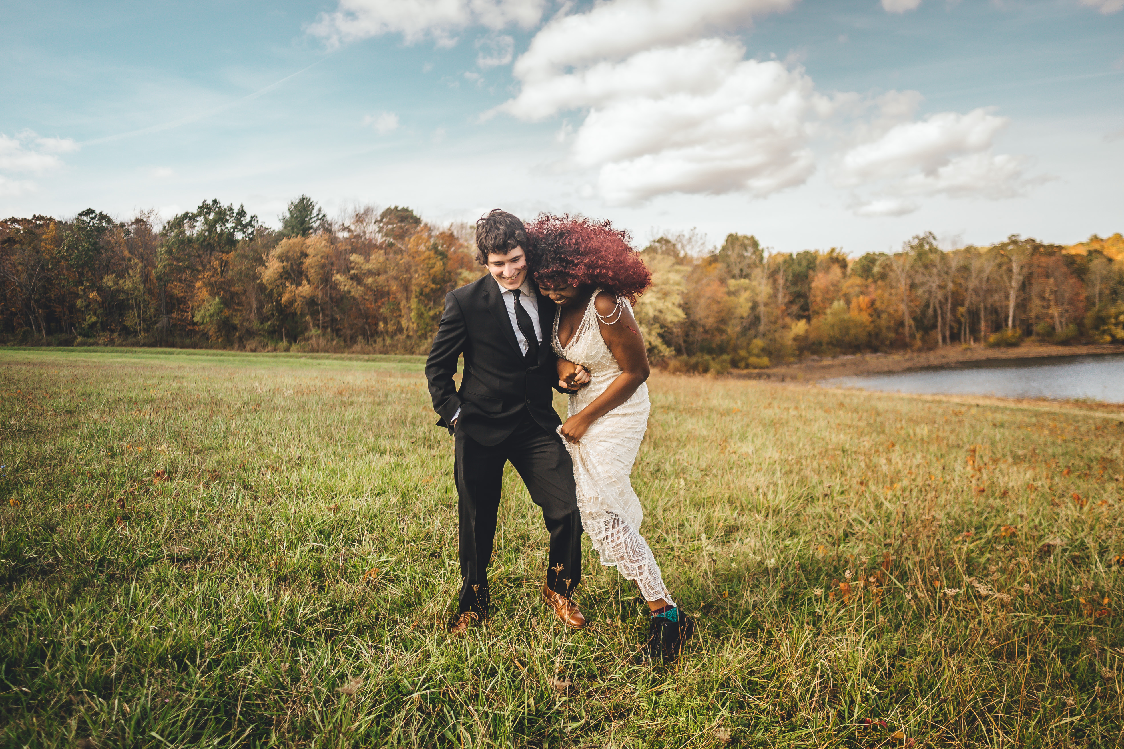 The groom in a black suit and the bride in a white lace dress with voluminous reddish-brown hair run together through an
