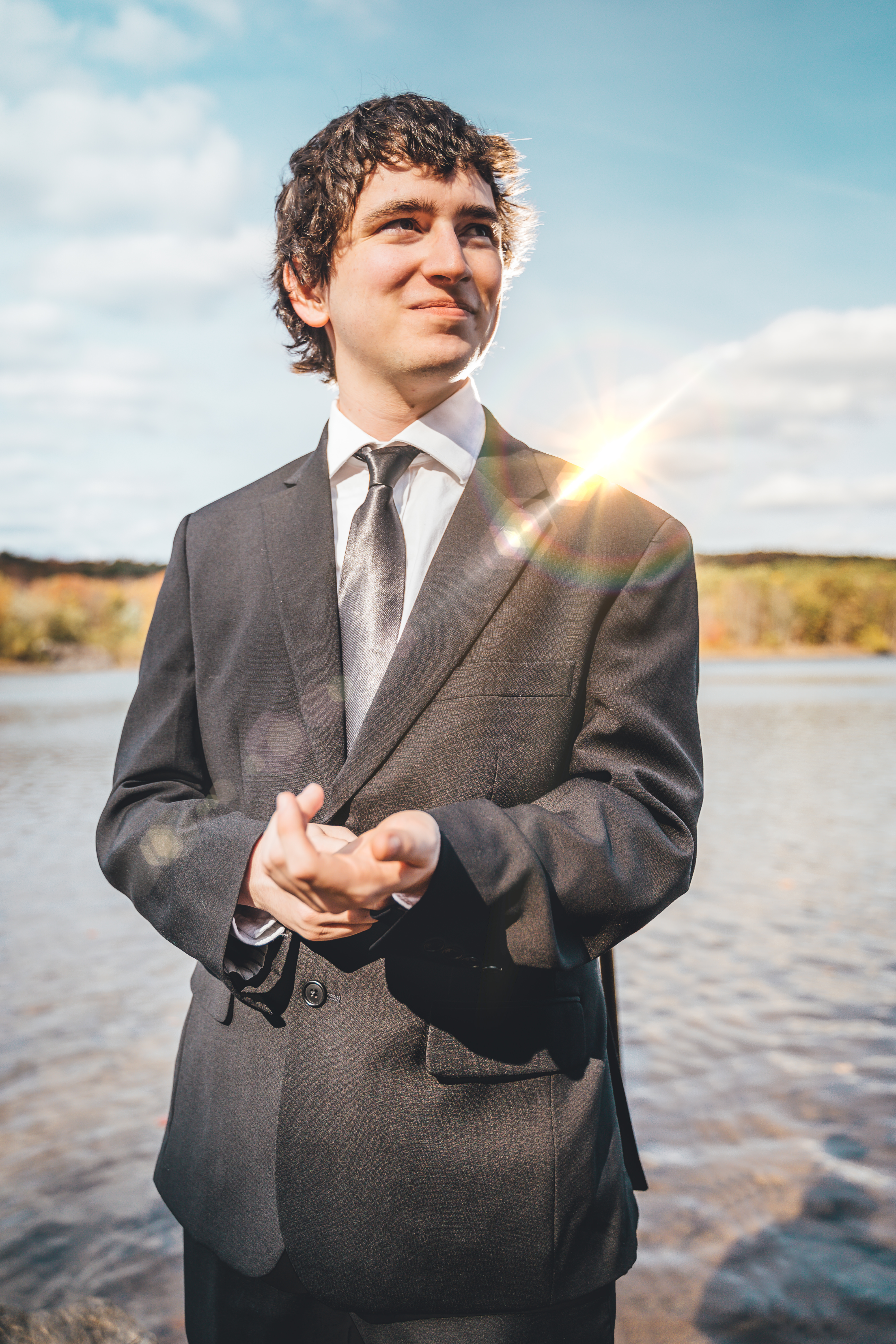Groom solo portrait standing on a sandy beach at golden hour, wearing a charcoal suit with white dress shirt and gray ti