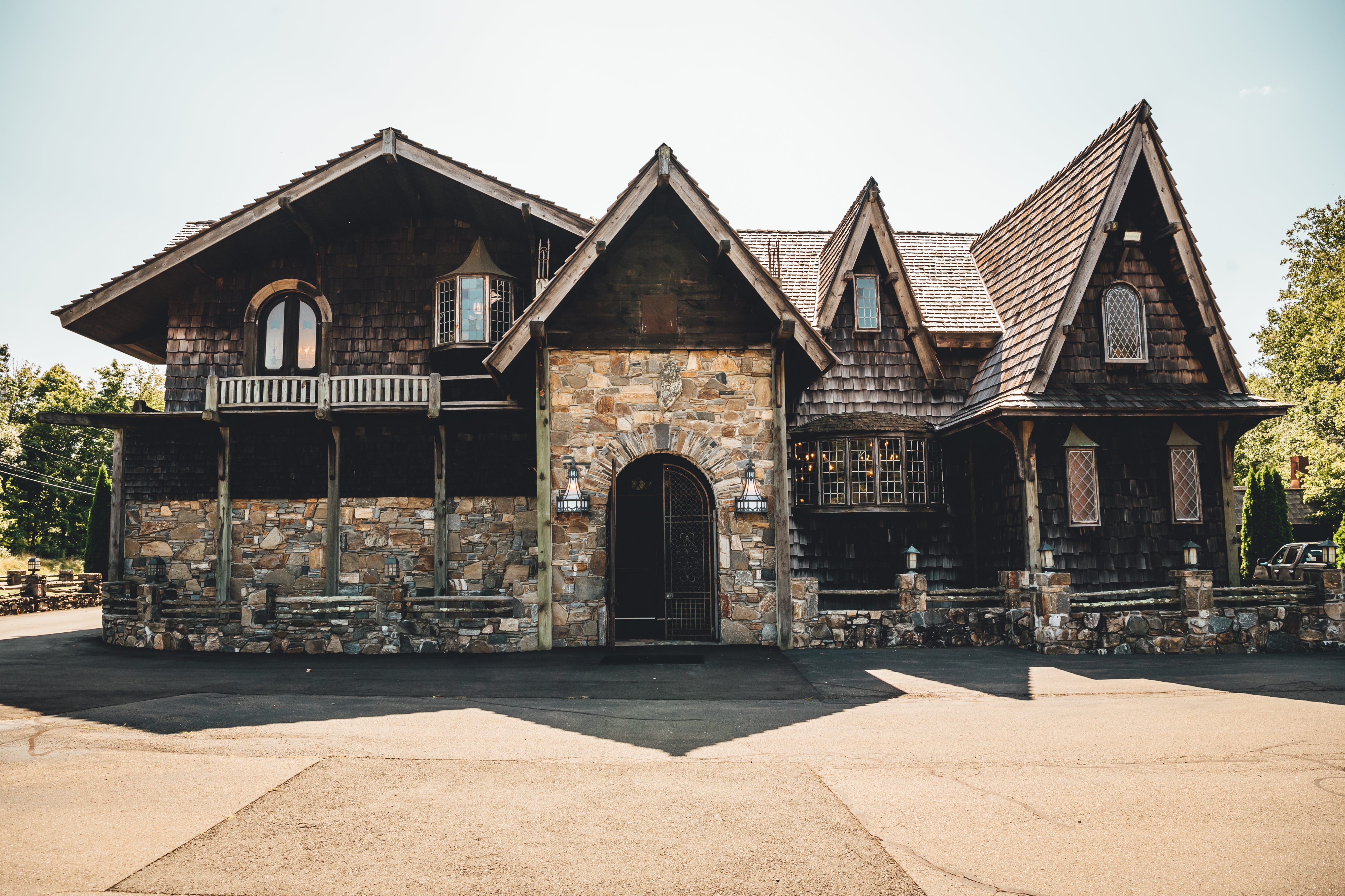 A striking dark stone and timber gothic-style venue building with multiple peaked roofs, arched doorway, and dramatic architectural details. The structure featu