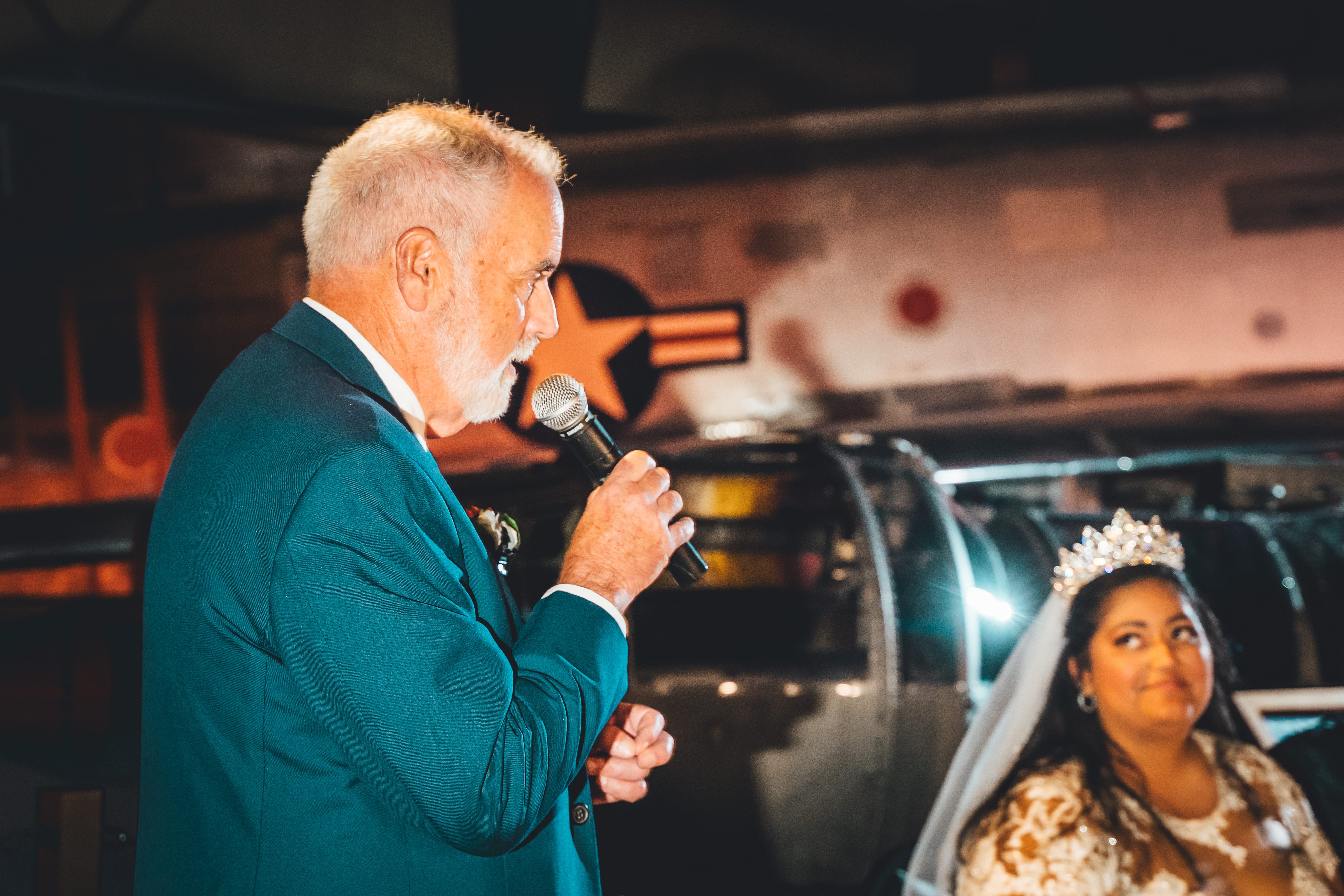 A wedding toast in front of a vintage aircraft, lit like a movie still