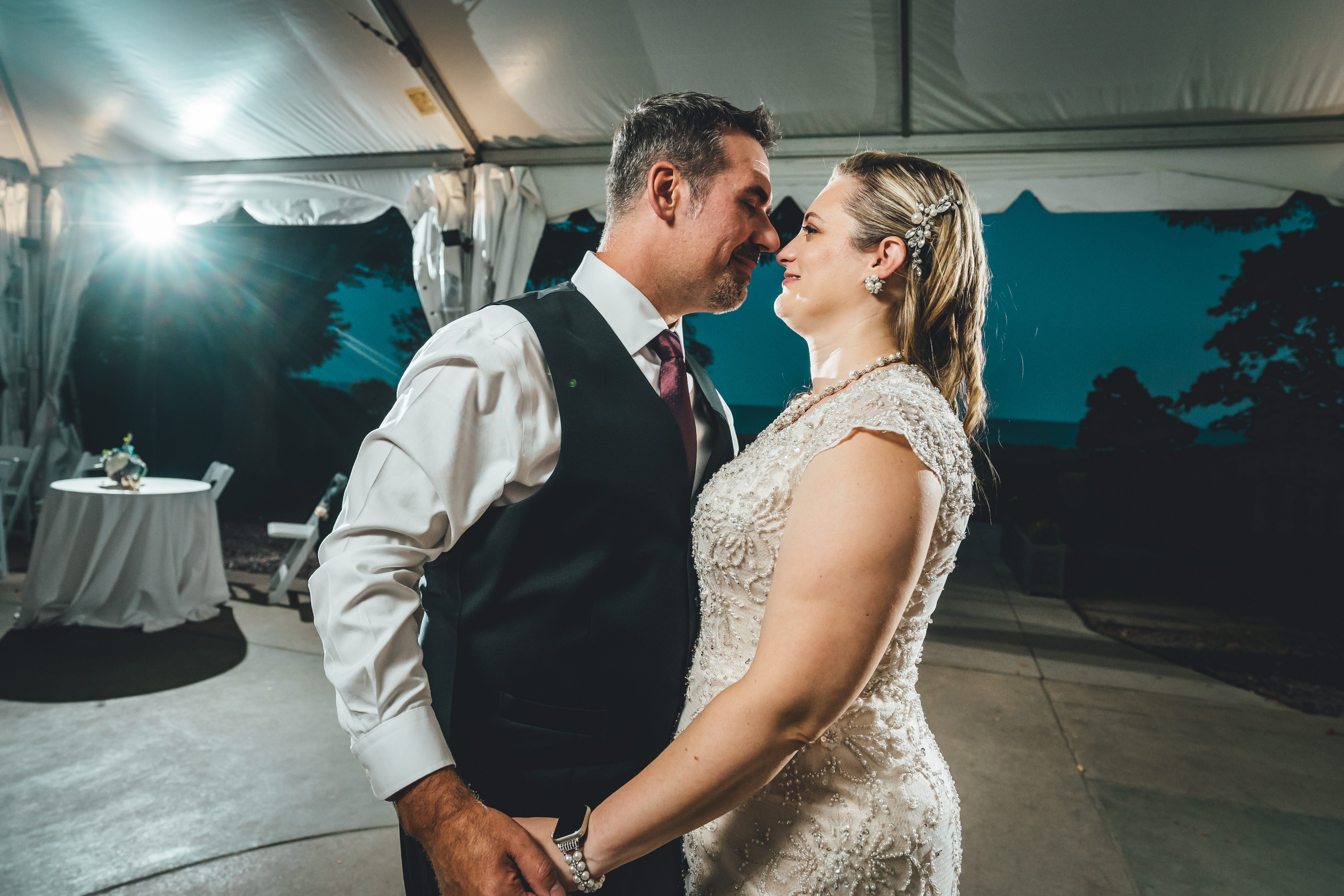 The bride and groom face each other intimately under a tent during their reception, holding hands and gazing at one another. A world map backdrop in teal and bl