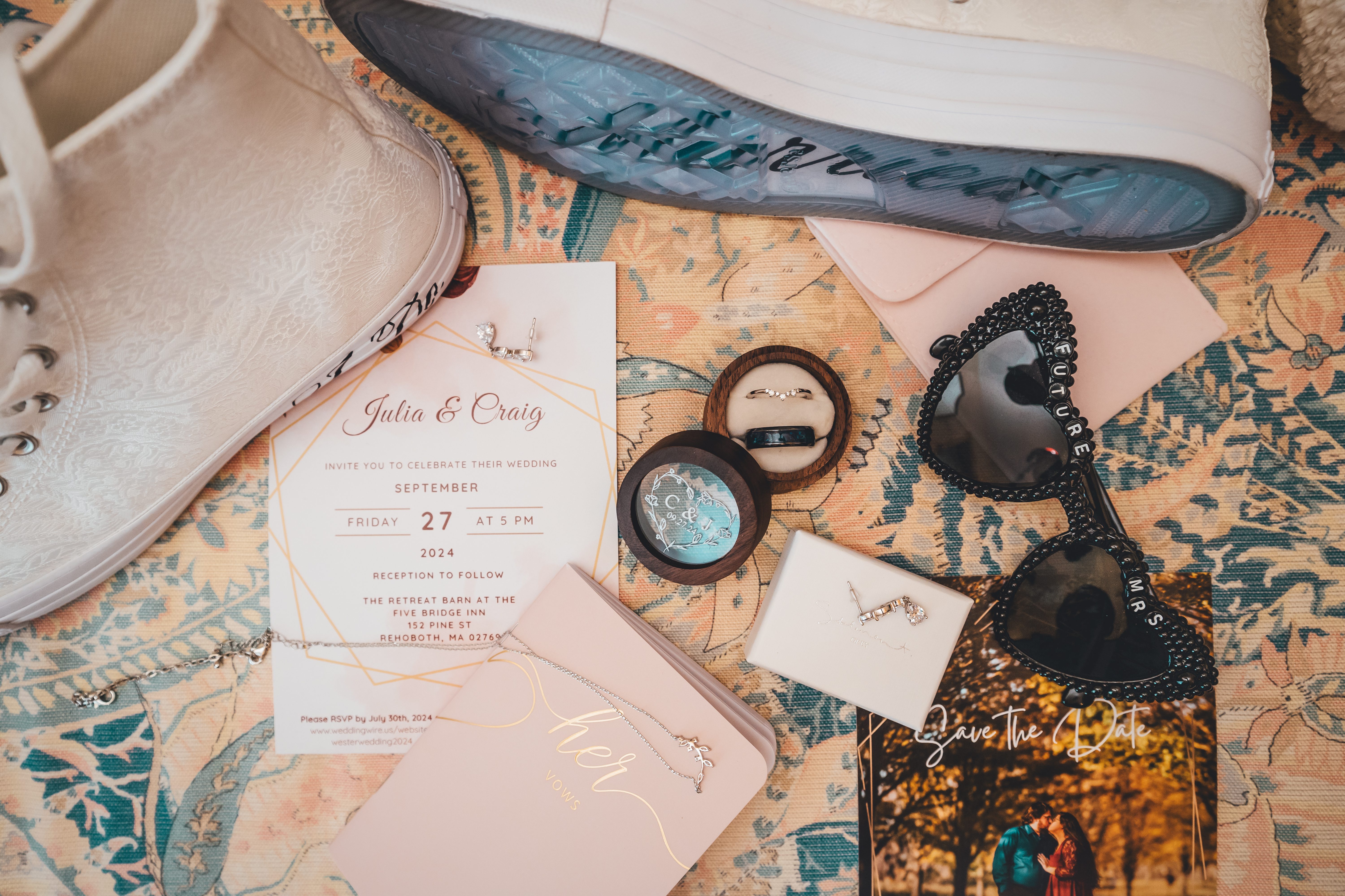Flat lay of wedding details including invitation, save-the-date, rings in wooden boxes, jewelry, white lace-up boots, an