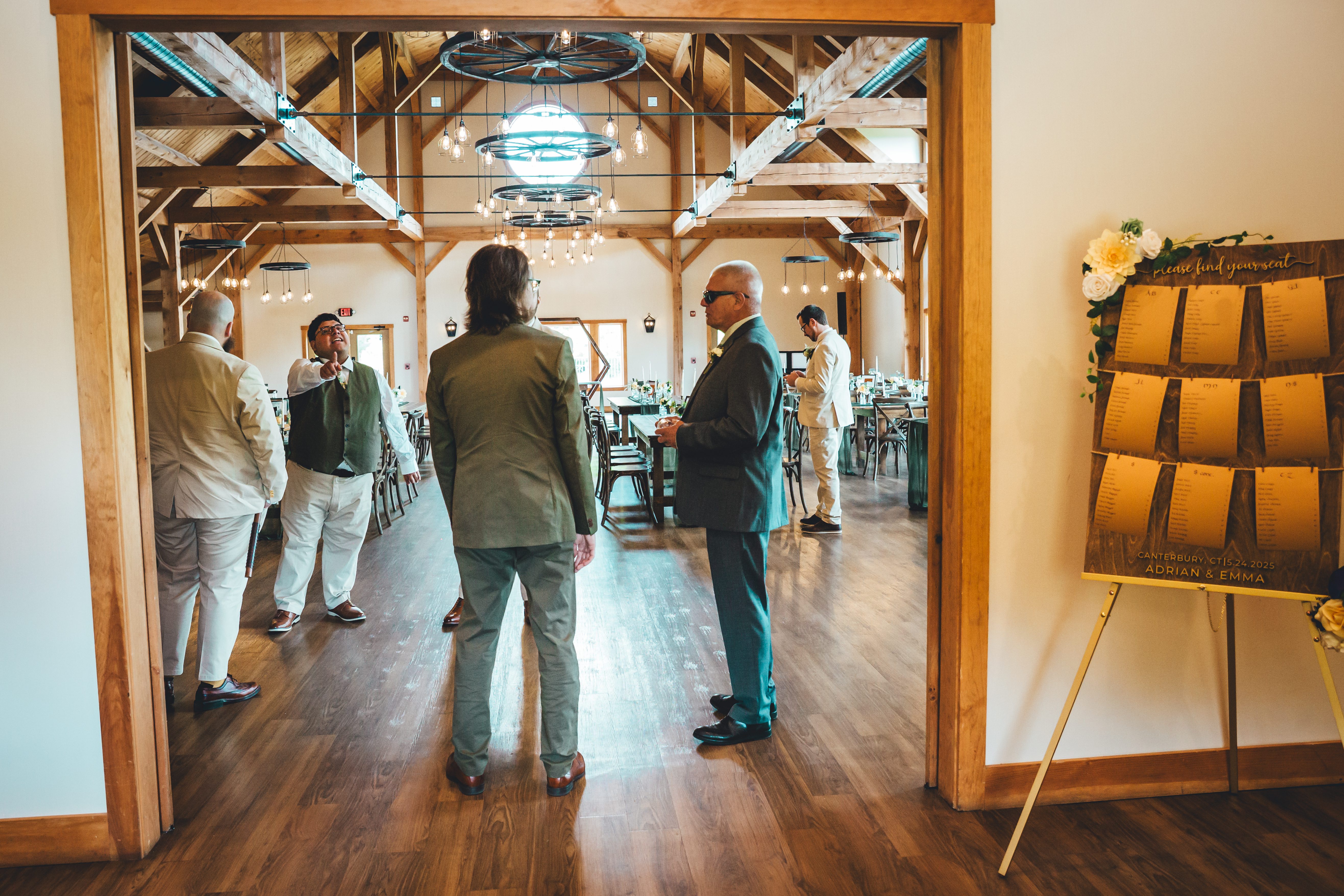 Guests mingle and socialize in a rustic barn reception space with exposed wooden beams and hanging pendant lights. The venue features a neon planet-shaped sign 
