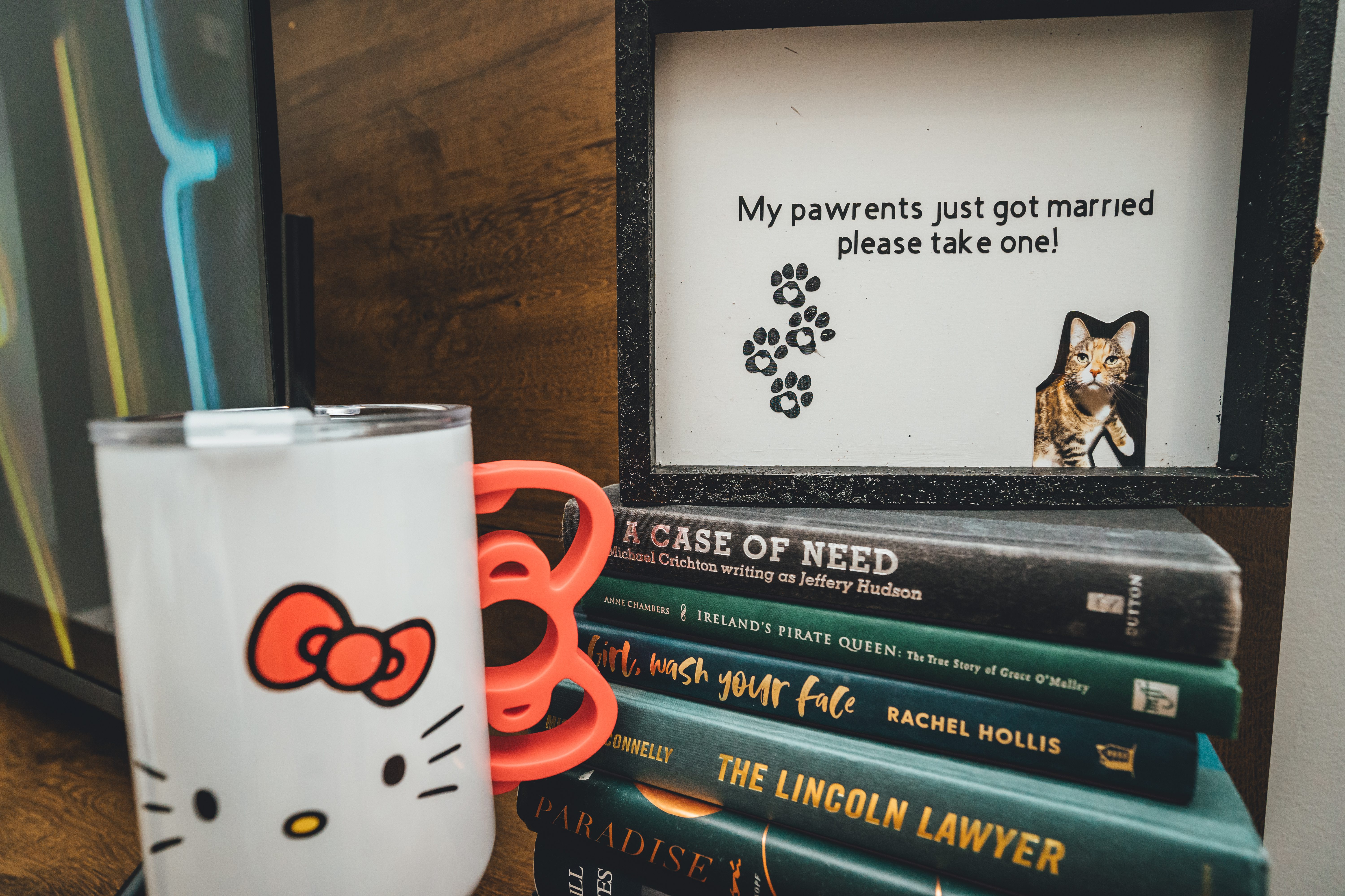 A styled detail shot featuring a Hello Kitty mug with red bow handle, a stack of literary books including titles by Rach