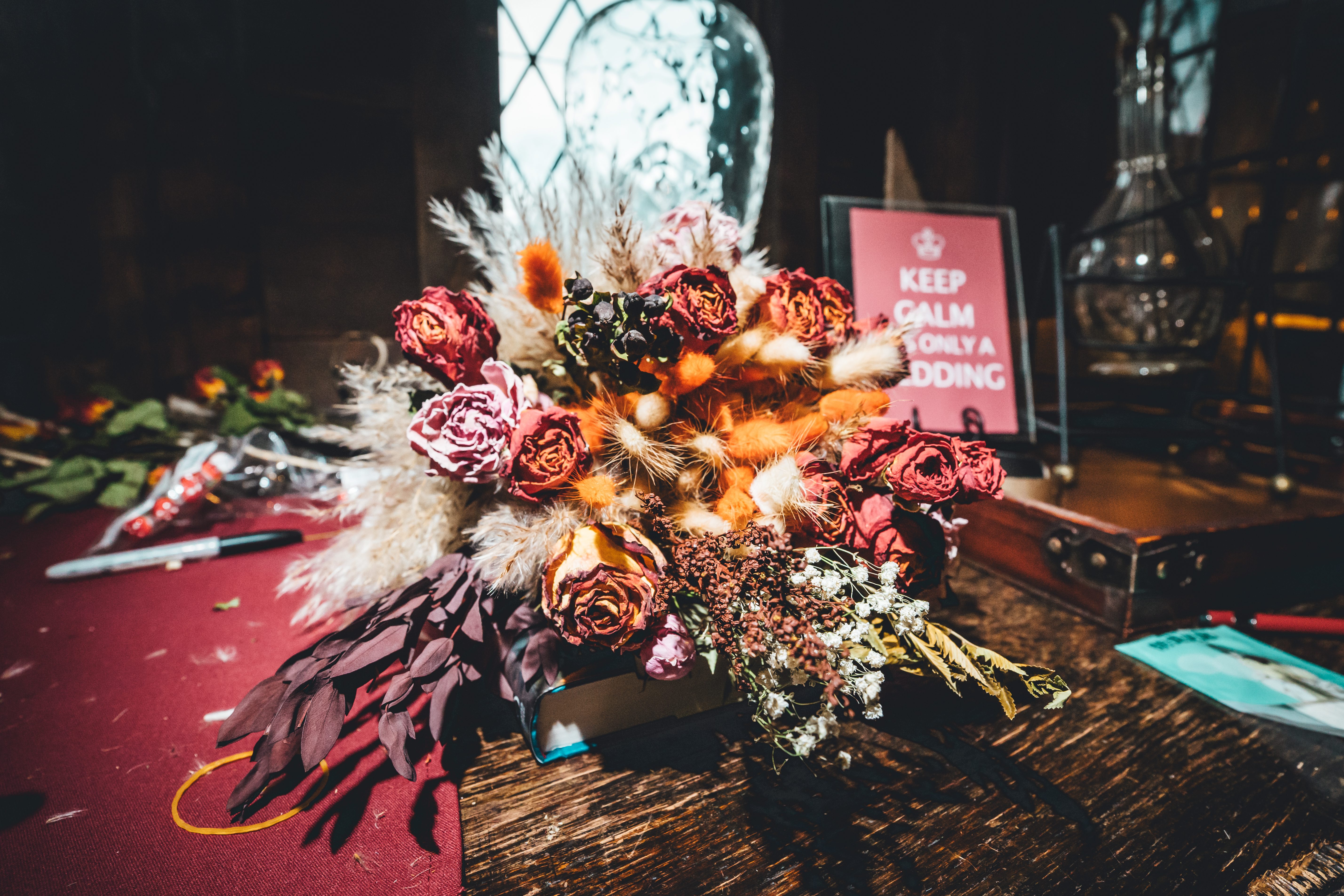 A striking wedding details shot featuring a lush bridal bouquet with burgundy roses, pampas grass, and feathered element