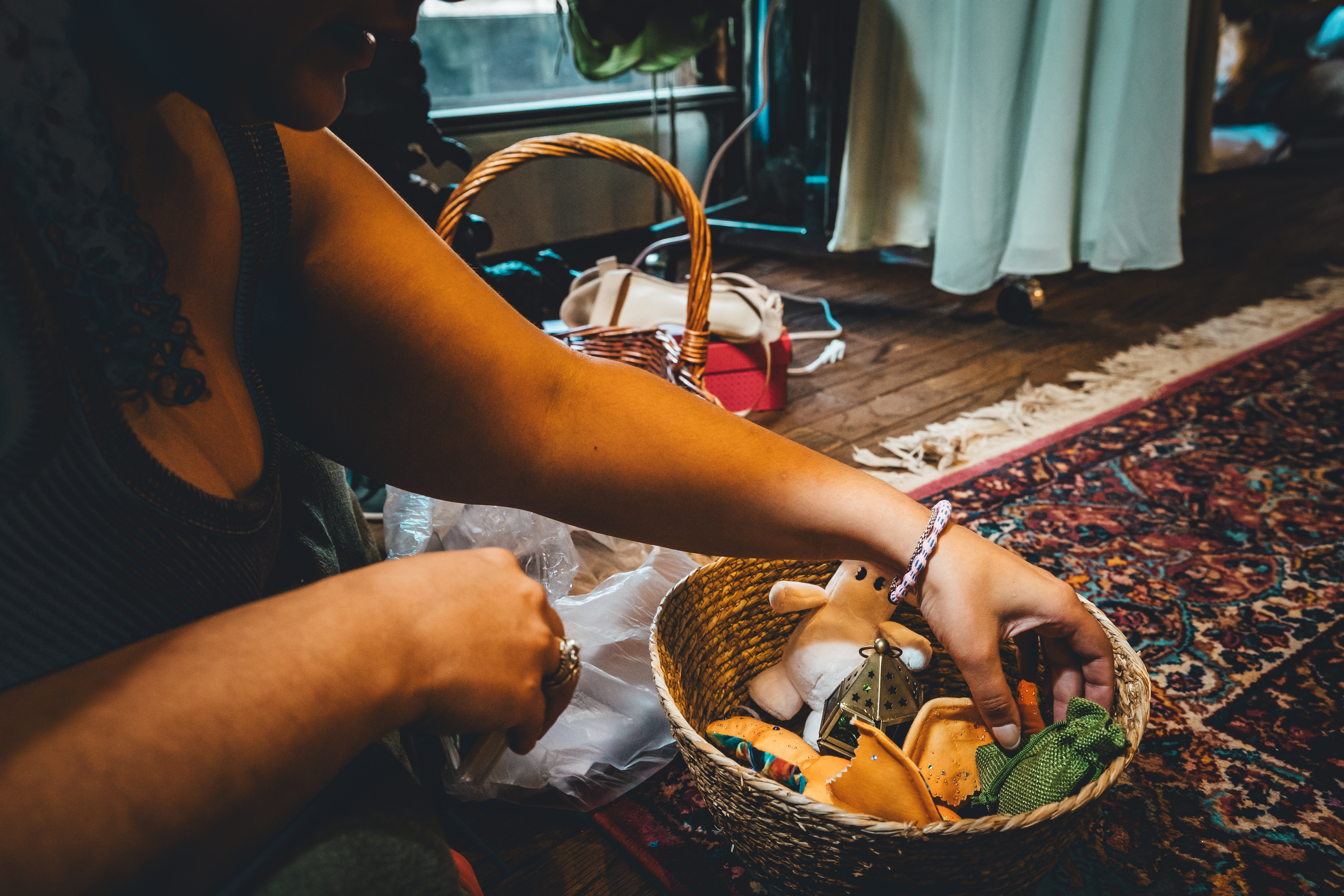 A person arranges items in a woven basket during getting-ready preparations. The basket contains various colorful objects including what appears to be a small b