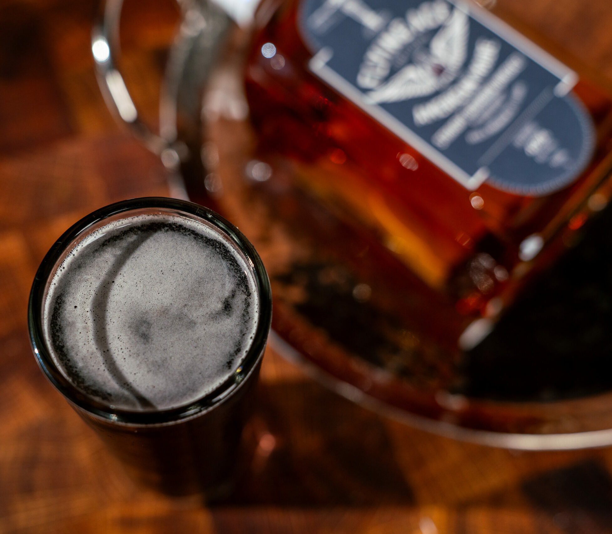 A dark side cocktail with black foam beside a bottle of whiskey