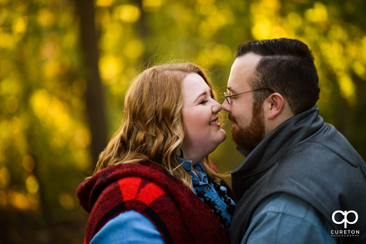 An engaged couple smiles nose to nose in an autumn forest