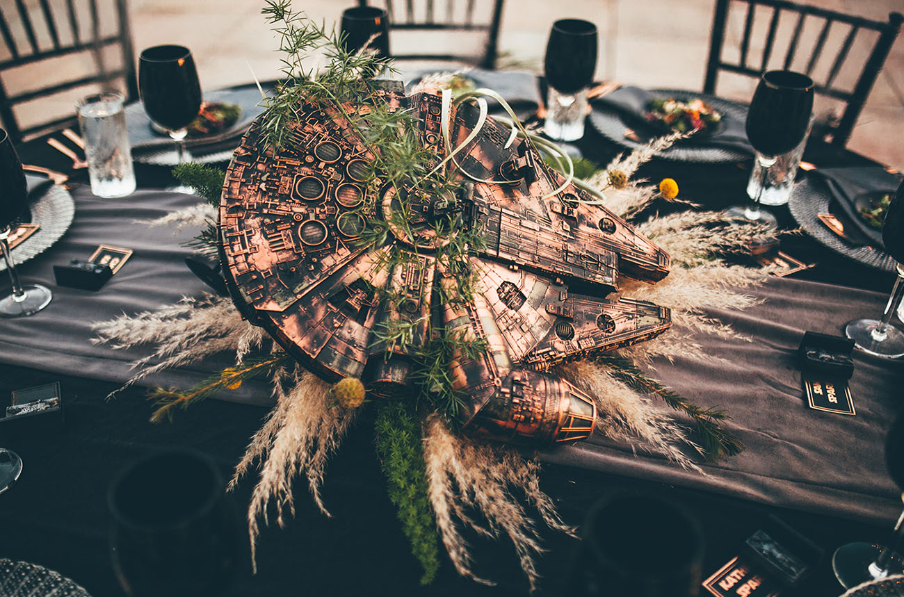 A copper Millennium Falcon centerpiece with greenery and pampas grass on a reception table