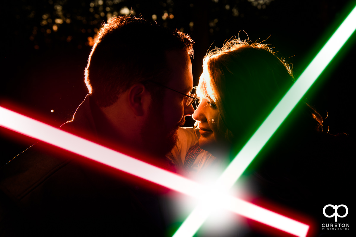 An engagement session portrait lit by crossed red and green lightsabers