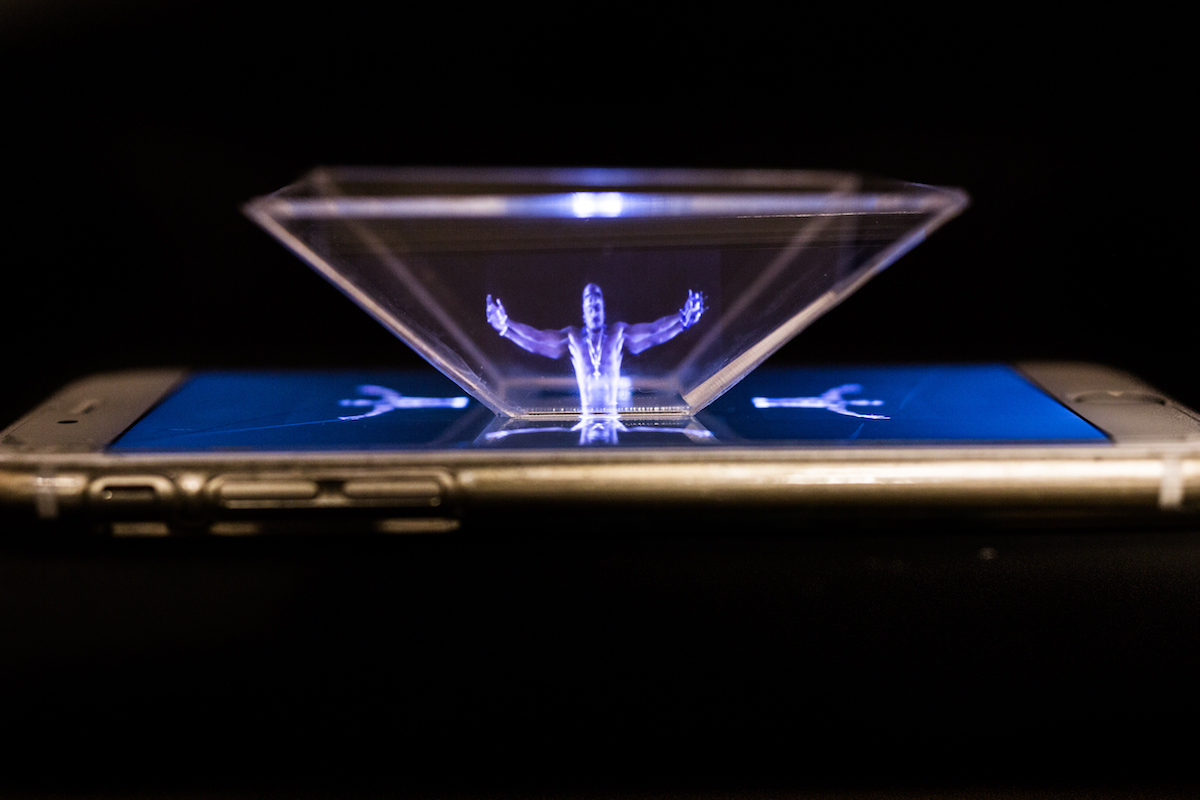 A CD-case pyramid on a smartphone projects a glowing hologram figure