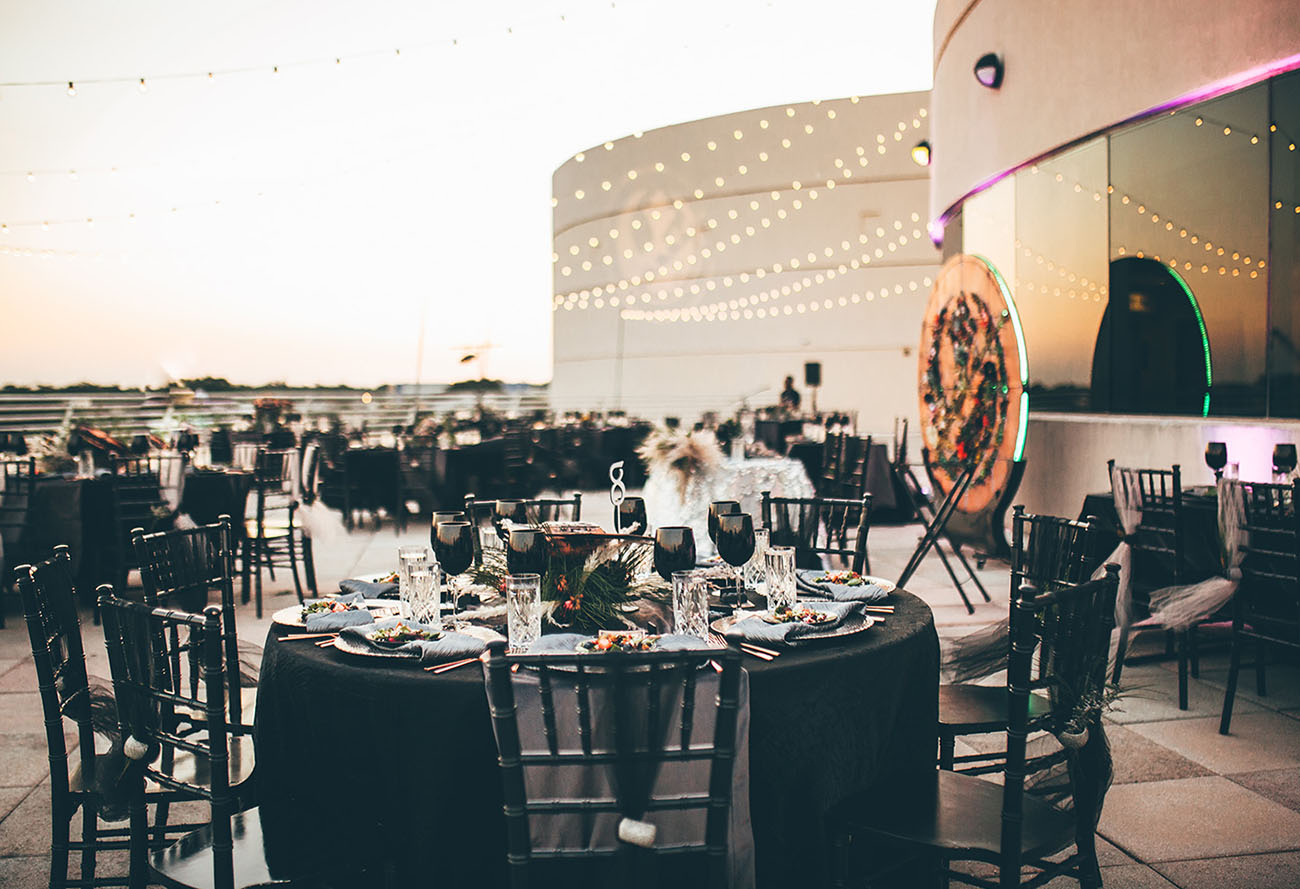 A rooftop Star Wars wedding reception with black linens and string lights at sunset